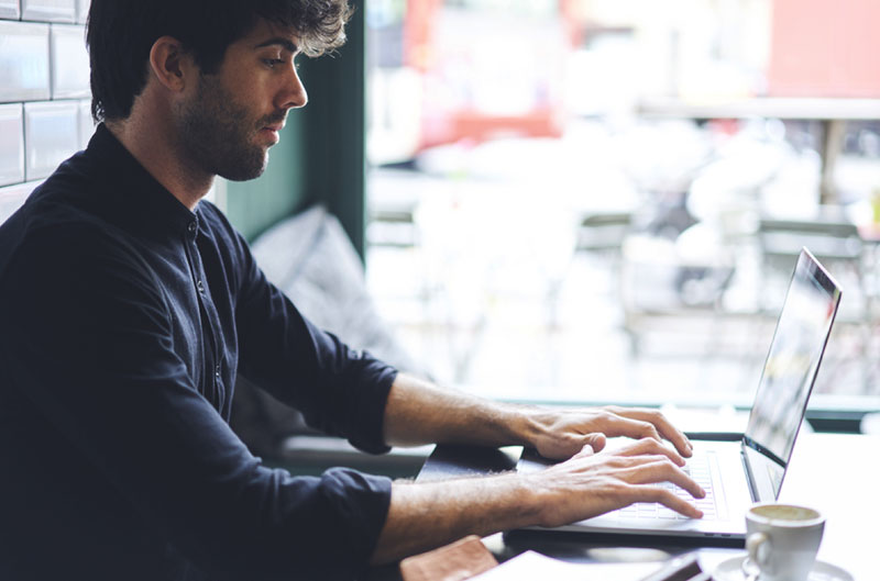 man typing on laptop at a cozy cafe table