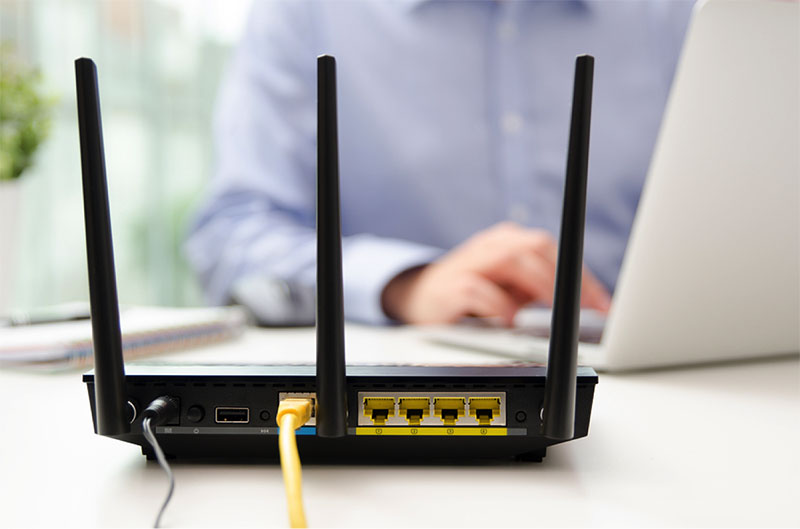 router connected with ethernet cable on desk, person working on laptop