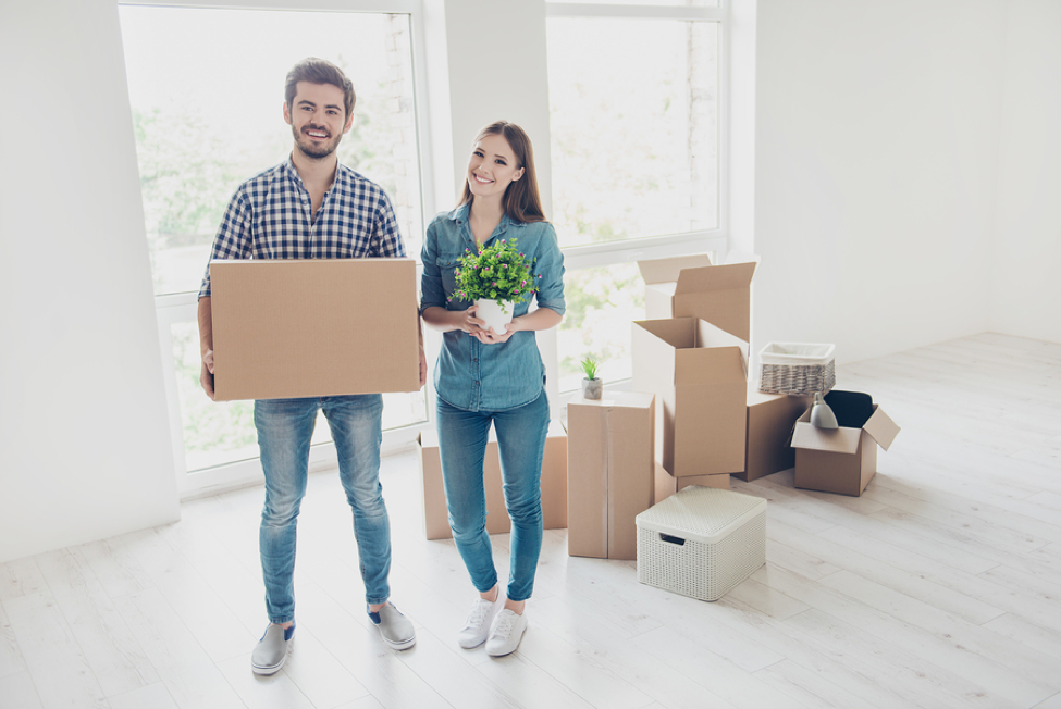 couple holding boxes and plant in bright, newly unpacked room