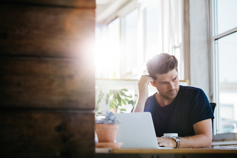 man thinking at laptop in sunlit office space.