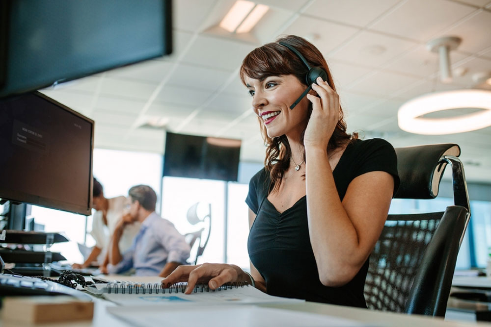 woman smiling, wearing headset, working in modern office setting.