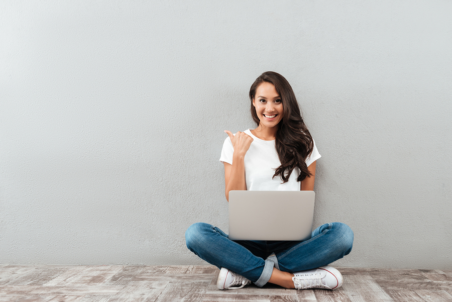 woman sitting cross-legged using laptop, smiling in casual setting.