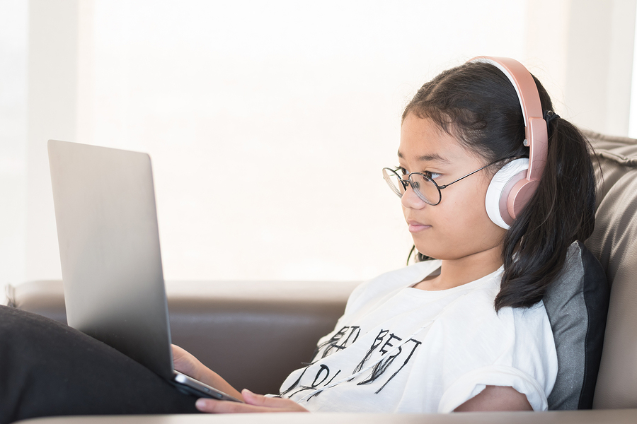 girl wearing headphones using laptop on couch
