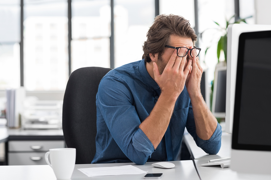 person rubbing eyes while sitting at office desk.