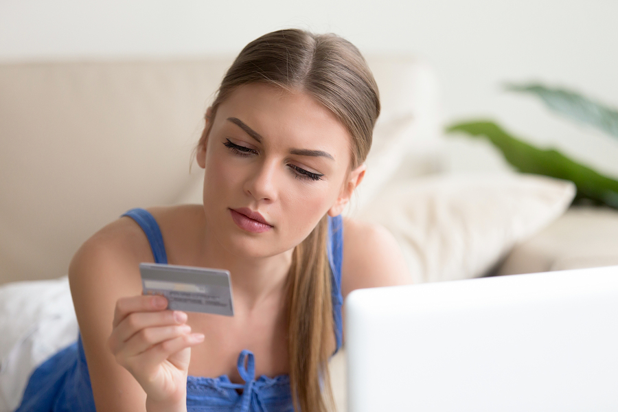 woman examining credit card near laptop on couch