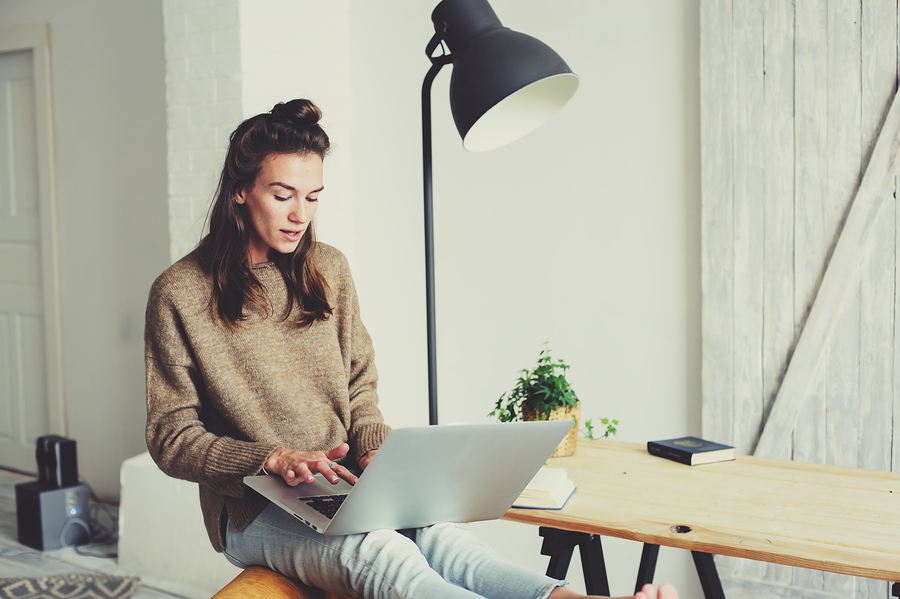 person working on laptop while sitting on desk at home