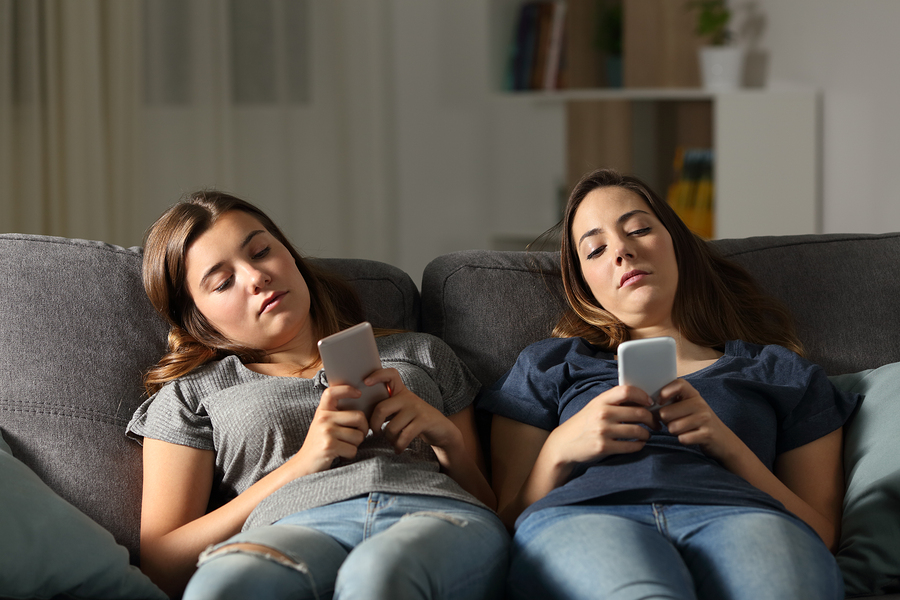 teenagers relaxing on couch, scrolling phones in dim living room