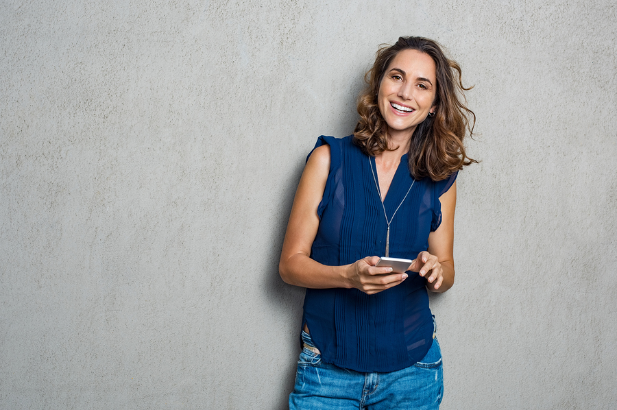 woman holding phone, smiling against a rough wall backdrop