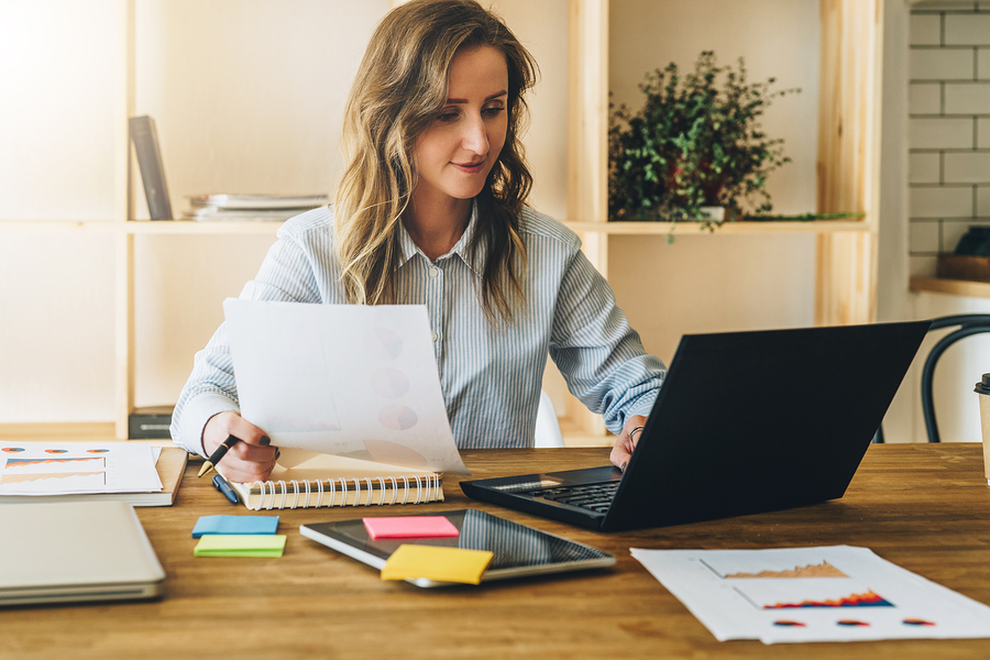 woman reviewing documents on laptop at wooden desk.