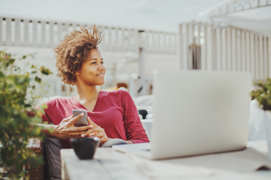 woman relaxing with phone outdoors near laptop, looking content