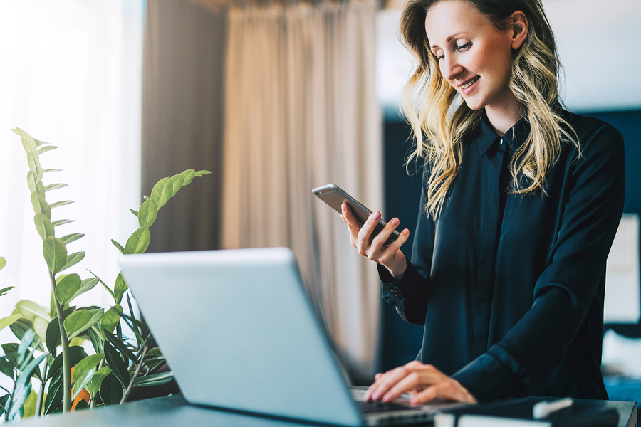 woman using smartphone while working on a laptop at home.