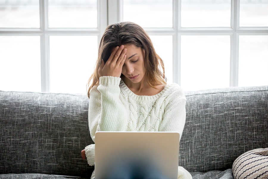 woman holding head, working on laptop, feeling stressed at home