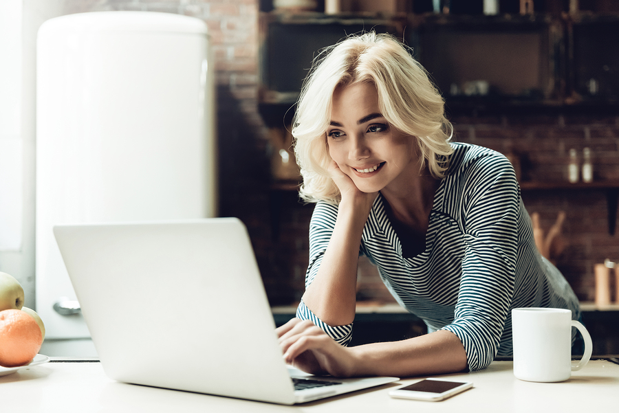 person smiling, using laptop in cozy kitchen setting