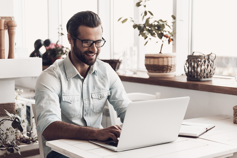 man typing on laptop, smiling in bright, modern workspace.