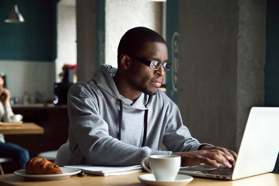 person in hoodie using laptop at cafe table with coffee