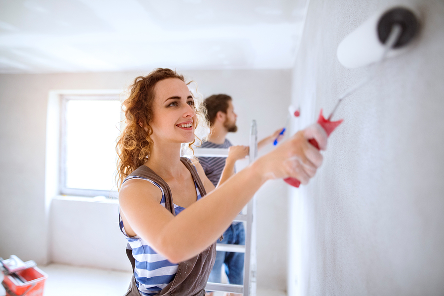 woman painting wall with roller alongside man in a bright room