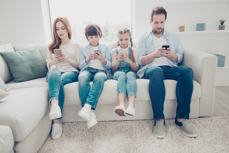 family using smartphones together seated on a cozy sofa.