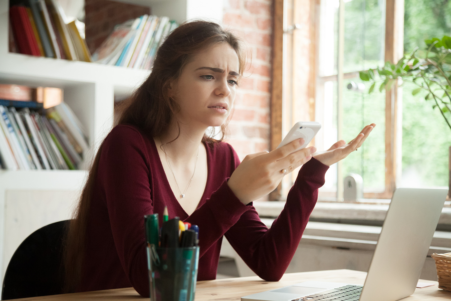 woman frustratedly looking at phone while working at desk