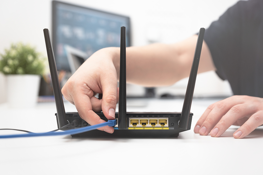hand connecting blue cable to a black router on a desk