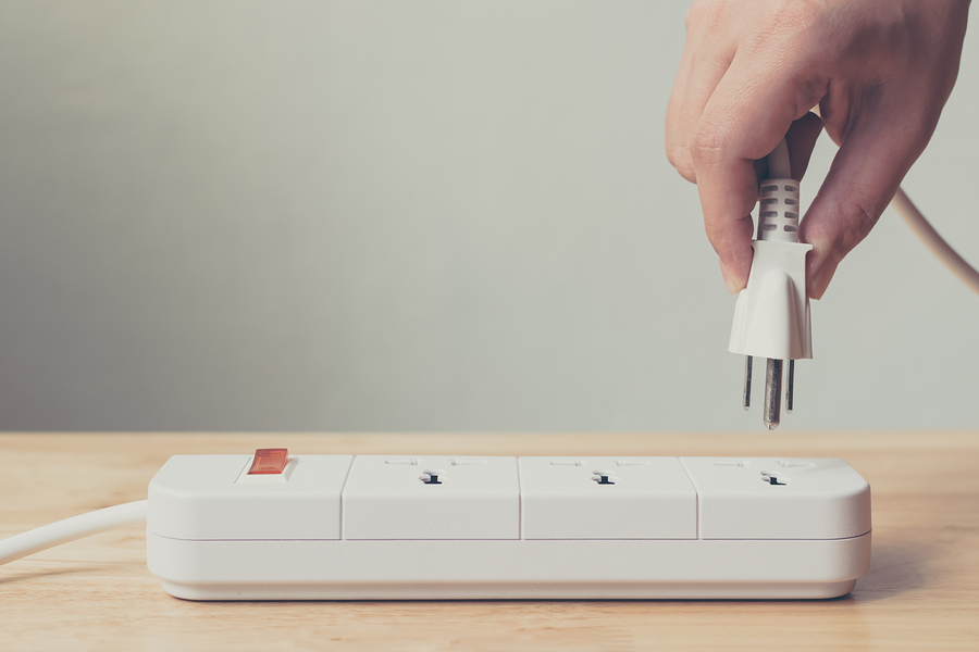 hand plugs cable into power strip on wooden table.