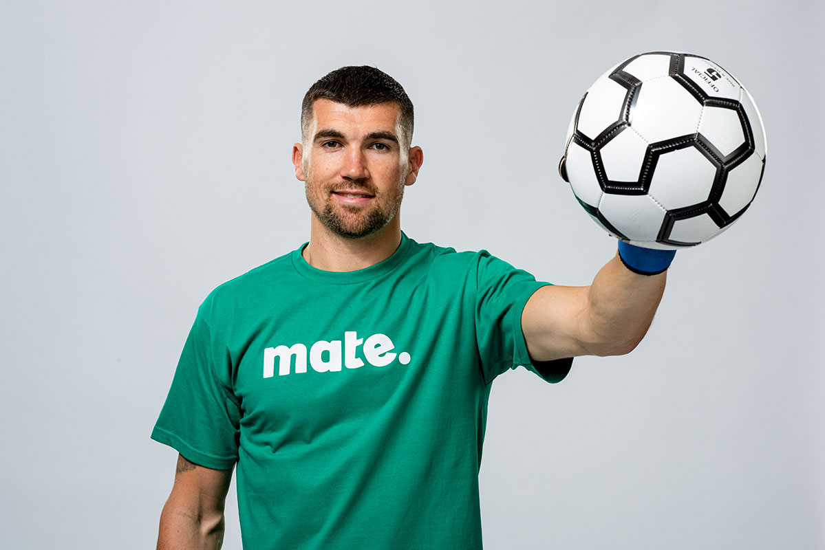 man holding soccer ball, wearing green mate shirt, smiling confidently