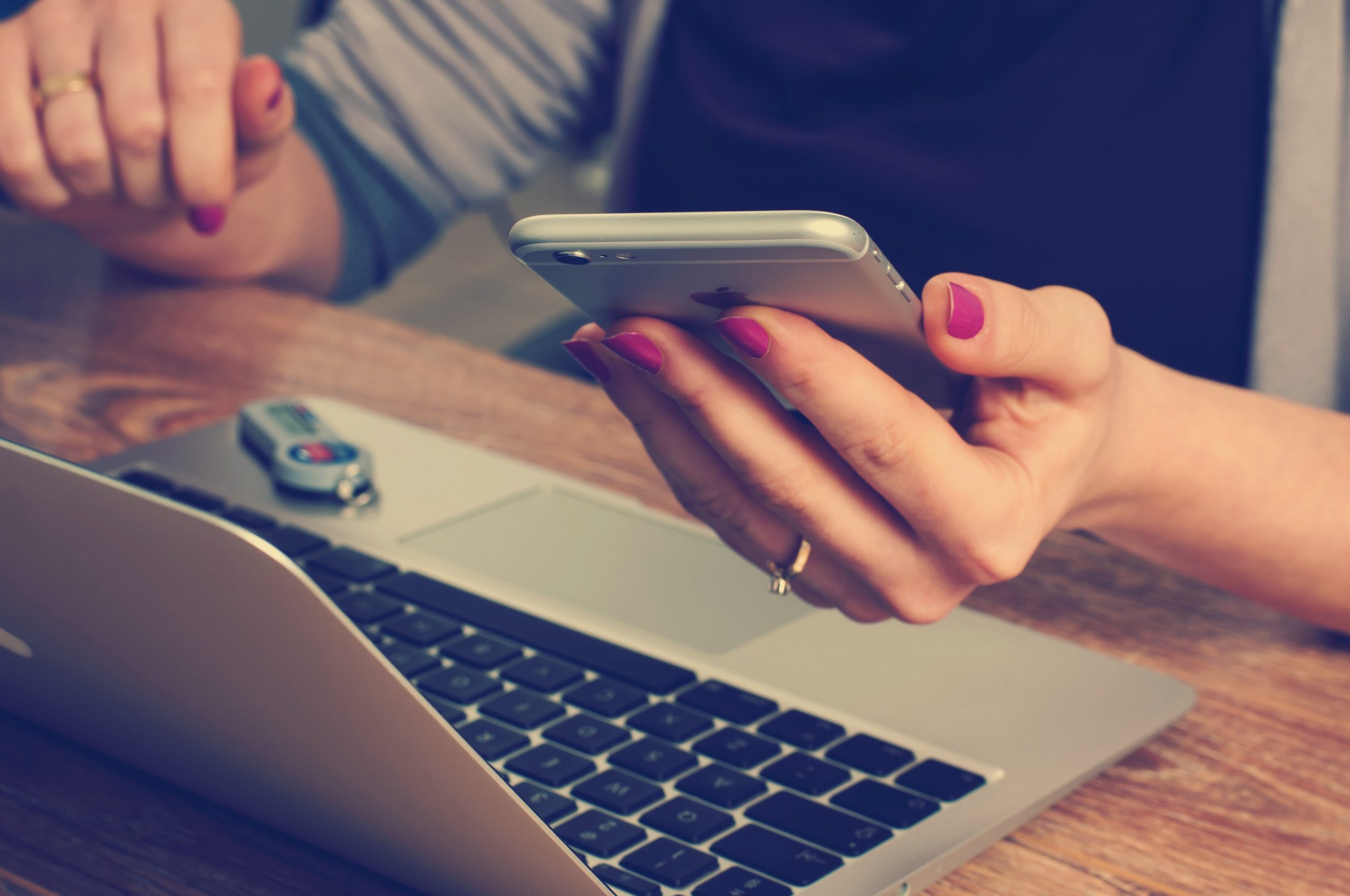 Woman holding smartphone while in front of laptop