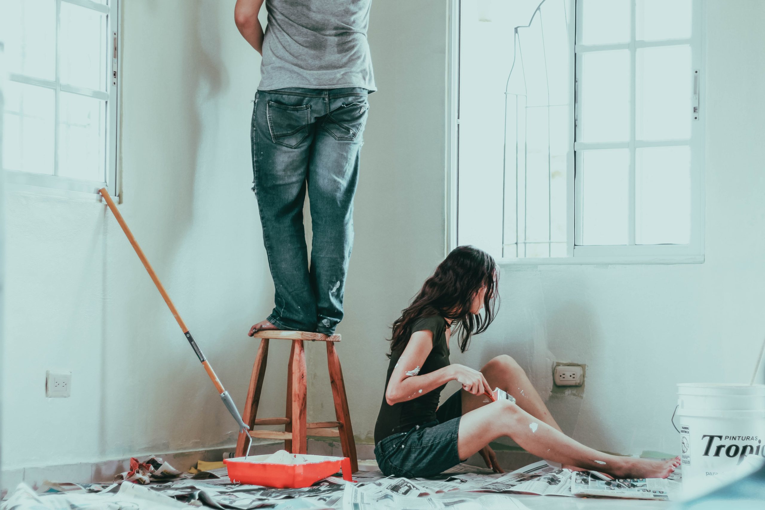 person paints wall while another sits on floor painting