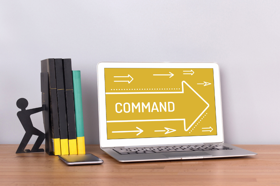 laptop displaying 'command' beside books and phone on desk