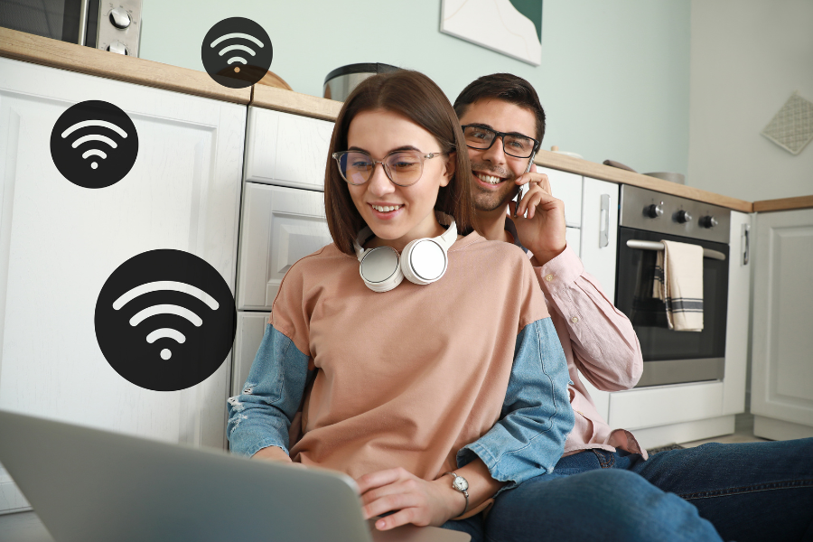 couple using laptop and phone in kitchen with wifi icons around