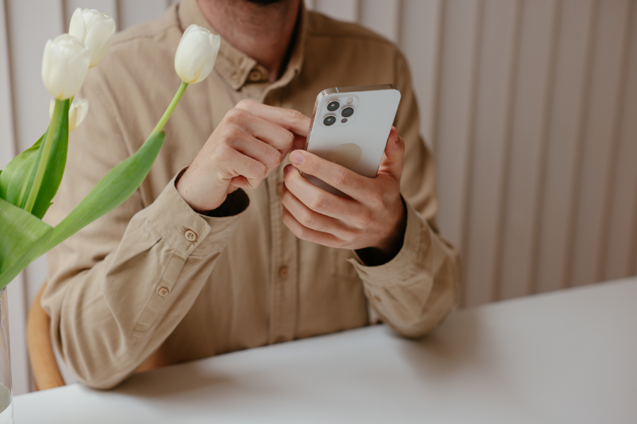 person using smartphone beside vase with tulips at table