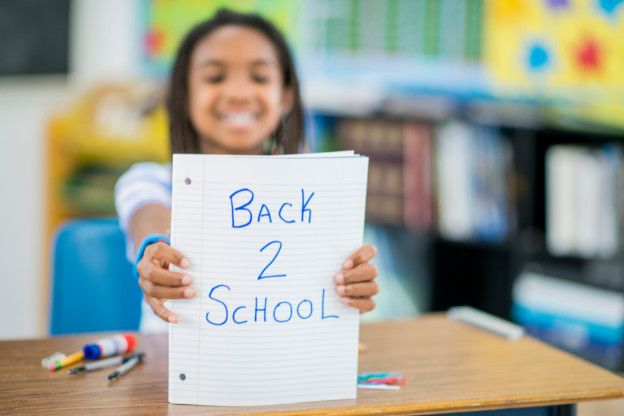 child holding back 2 school sign at a classroom desk.