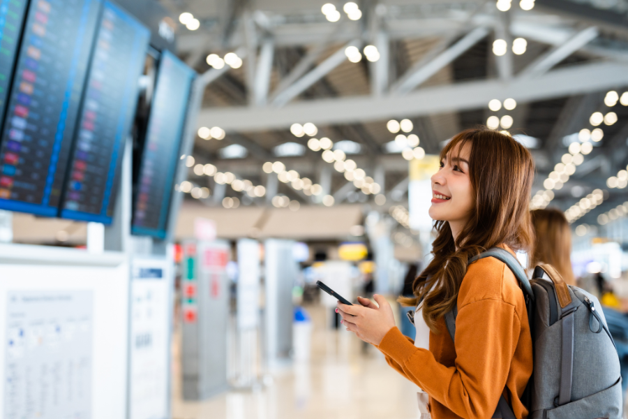 woman checking flight information at airport terminal with smartphone