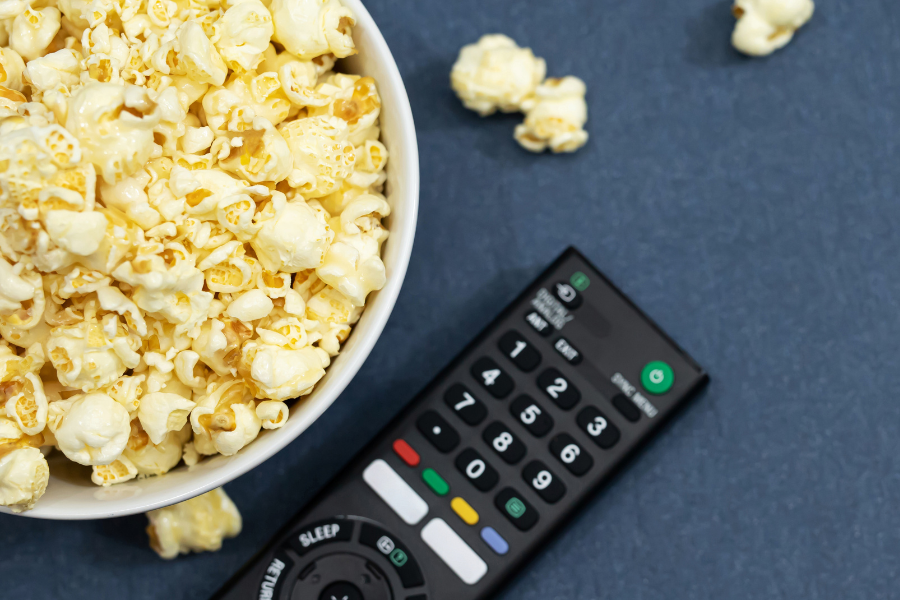 bowl of buttered popcorn beside remote on blue surface