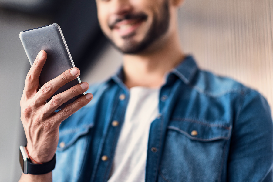 man smiling, holding smartphone, wearing denim jacket indoors.