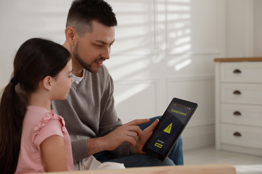 father demonstrating parental controls on tablet to daughter in living room.