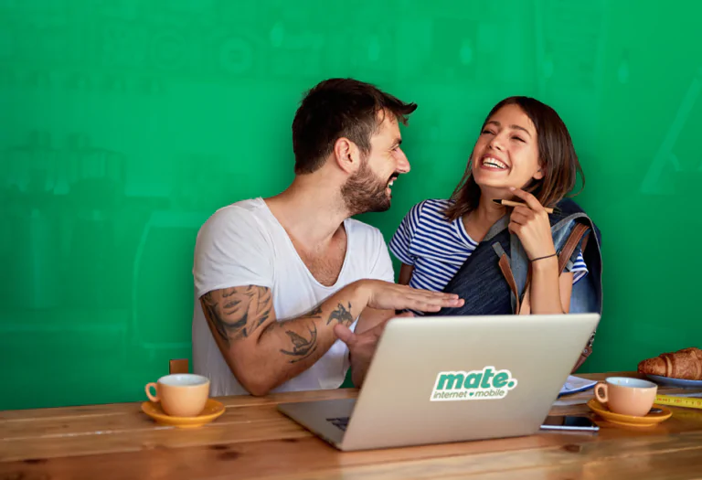 man showing something on laptop by the mate, laughing in cafe.